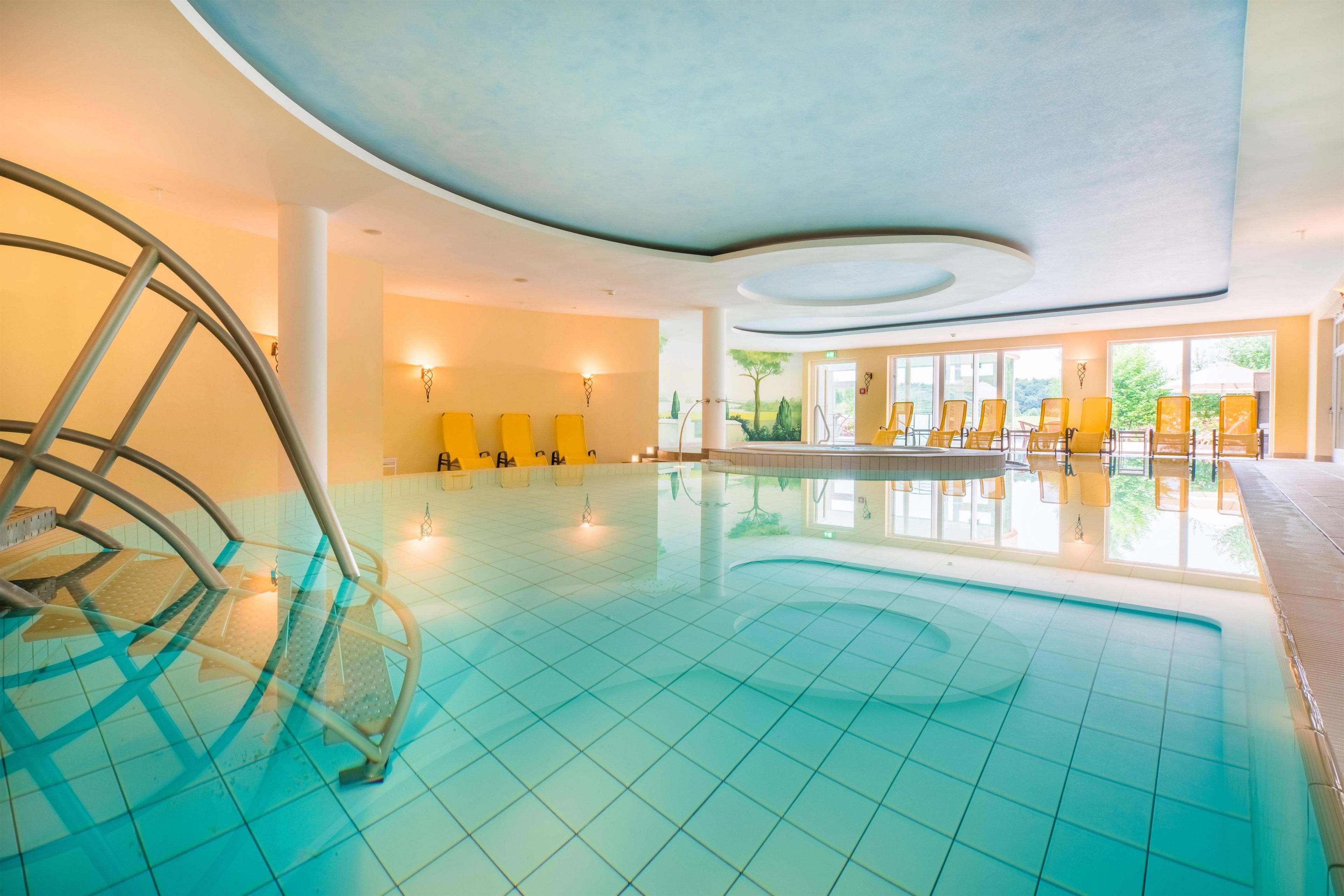 Una piscina interior con agua azul cristalina, sillas amarillas y un diseño moderno en el techo.