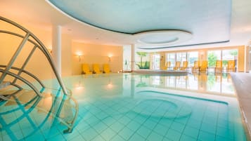 Una piscina interior con agua azul cristalina, sillas amarillas y un diseño moderno en el techo.