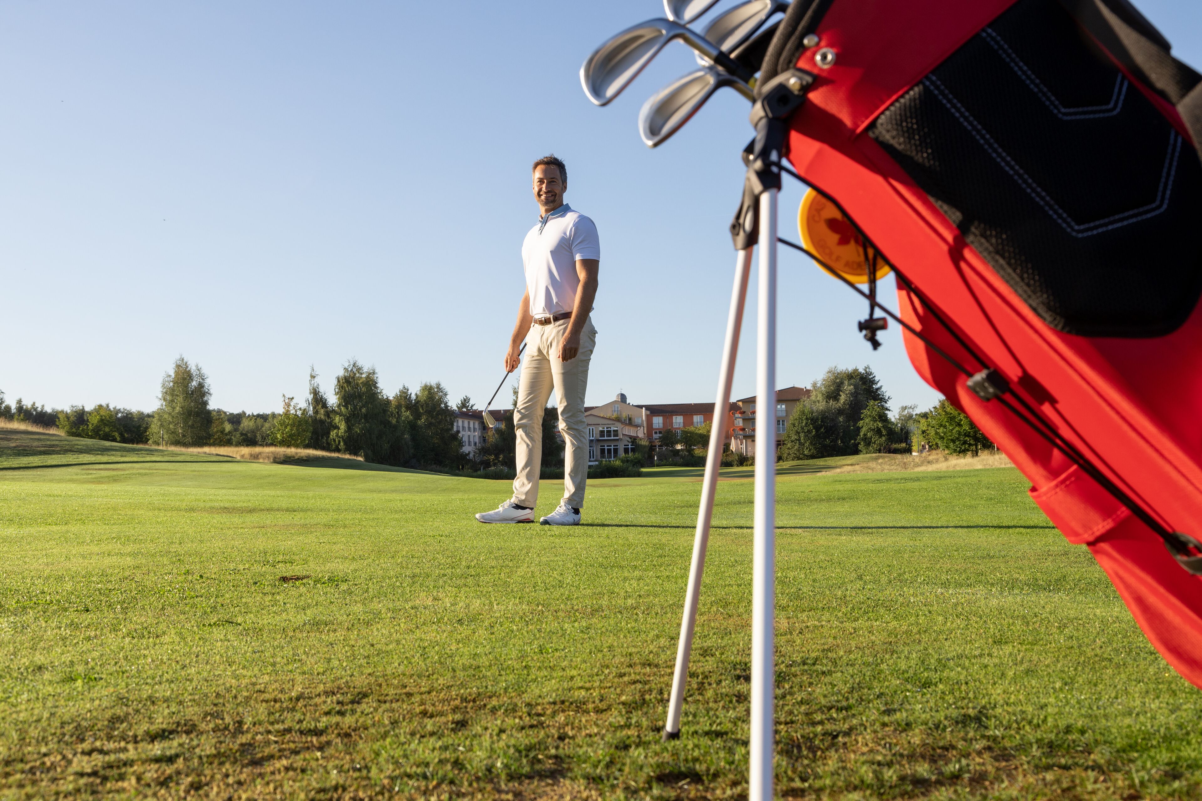 Een golfbaan met een persoon die bij een golfbag en clubs staat.
