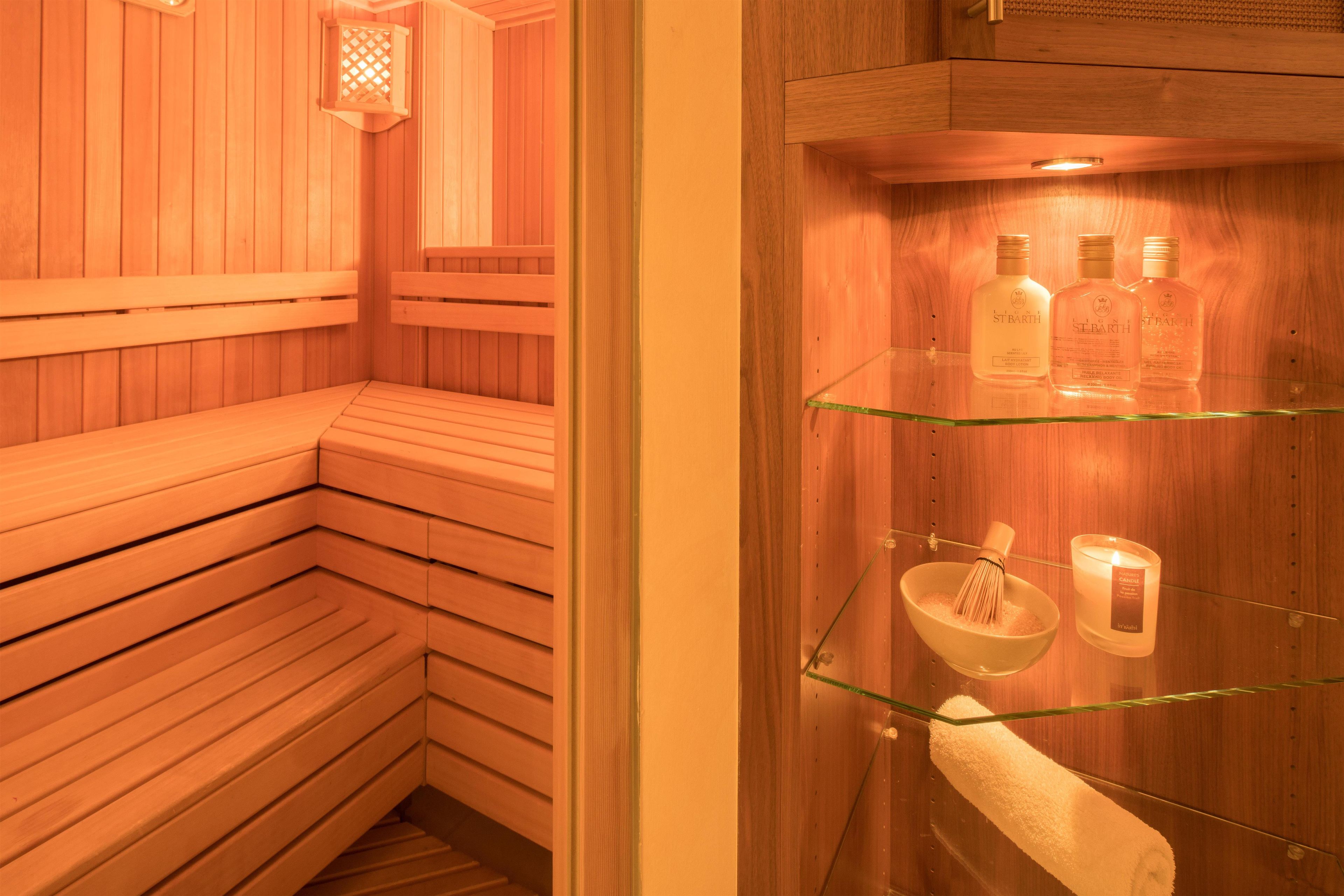 A sauna room with wooden benches and a glass shelf holding bottles and a candle.