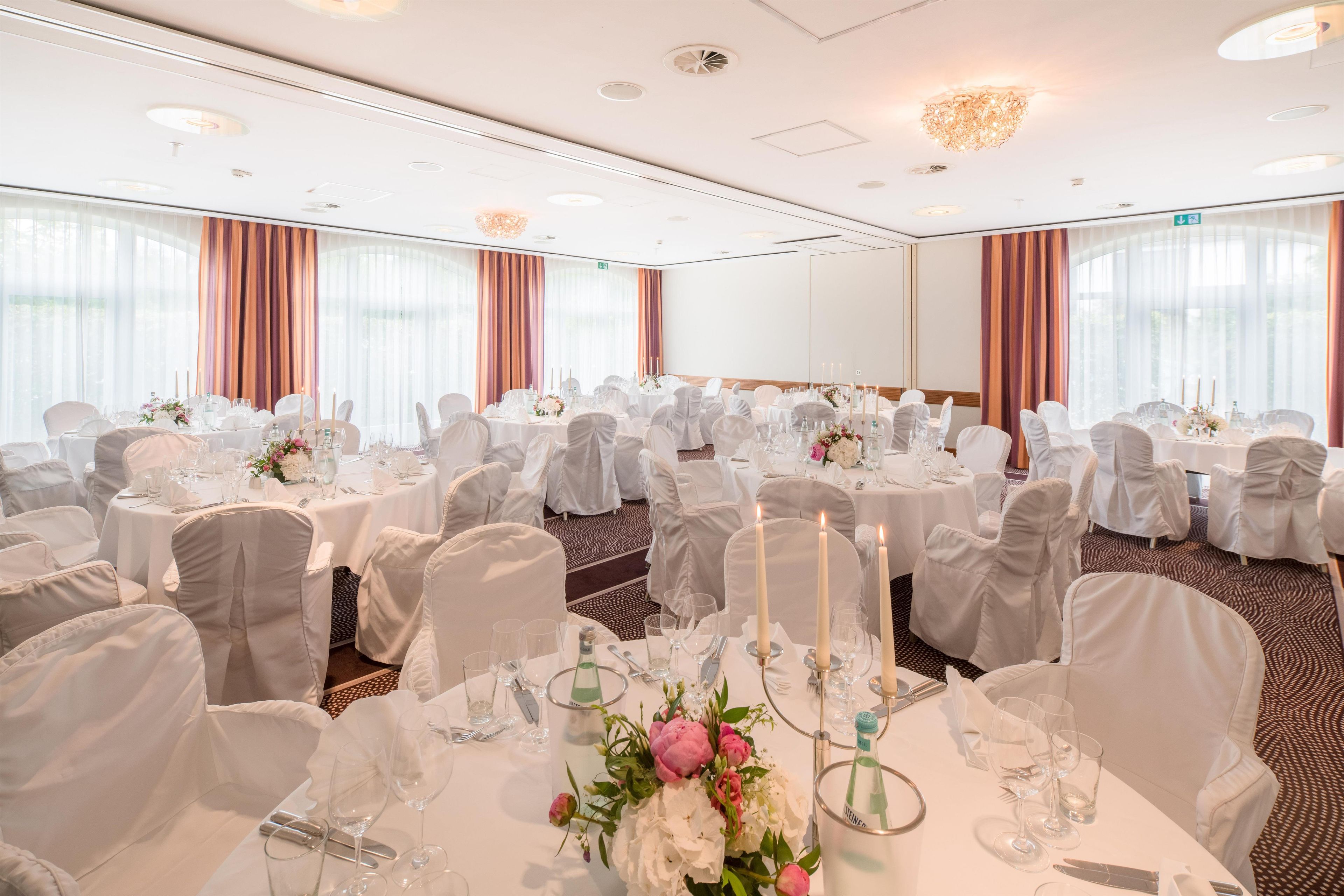 Une salle de banquet avec des tables rondes, des nappes blanches et des chaises.