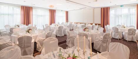 Une salle de banquet avec des tables rondes, des nappes blanches et des chaises.