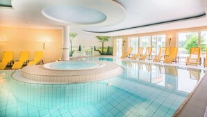 Una piscina con un hidromasaje circular, sillas de descanso amarillas y vistas a árboles a través de amplios ventanales.