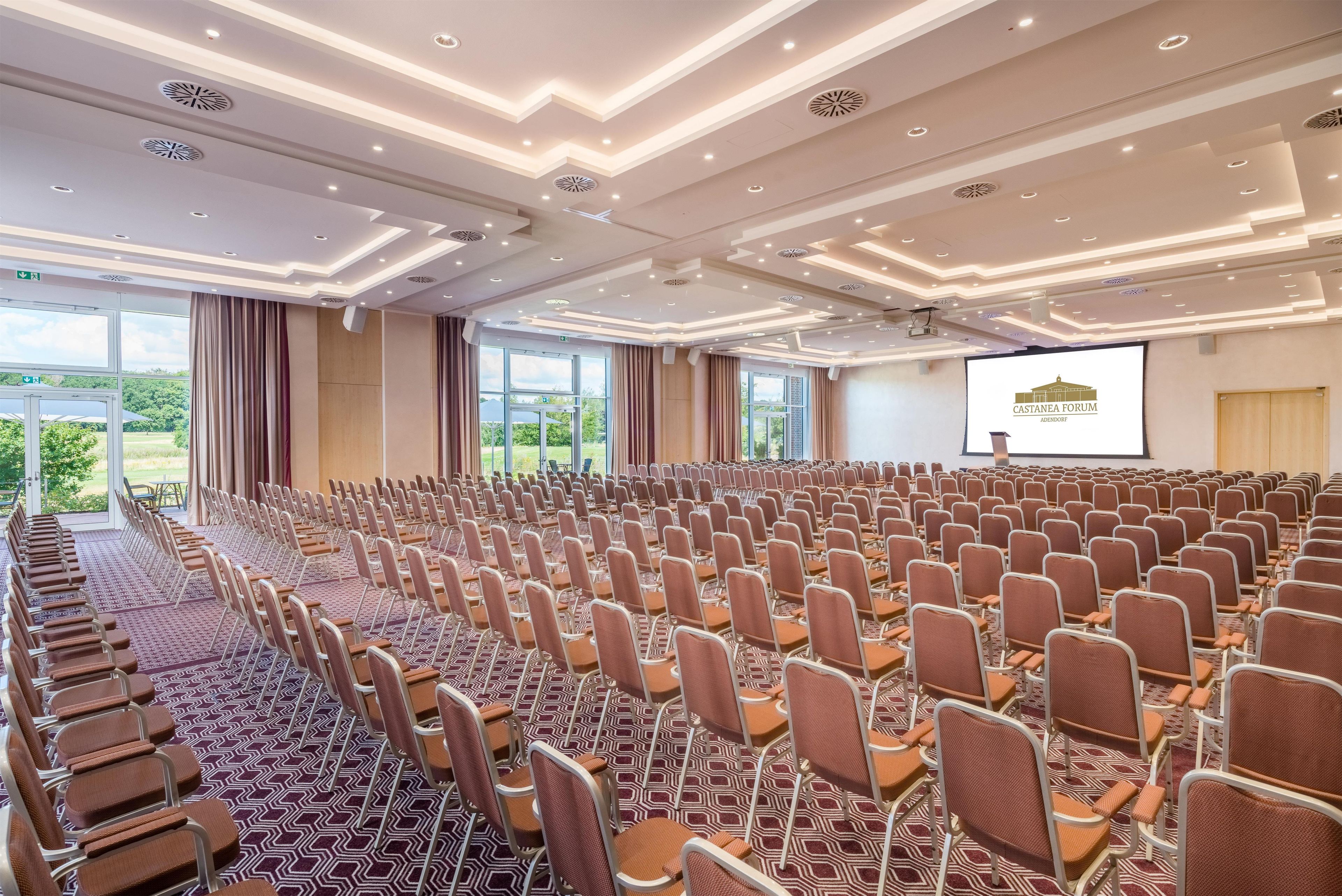 A conference room with rows of chairs, a projector screen, and large windows.