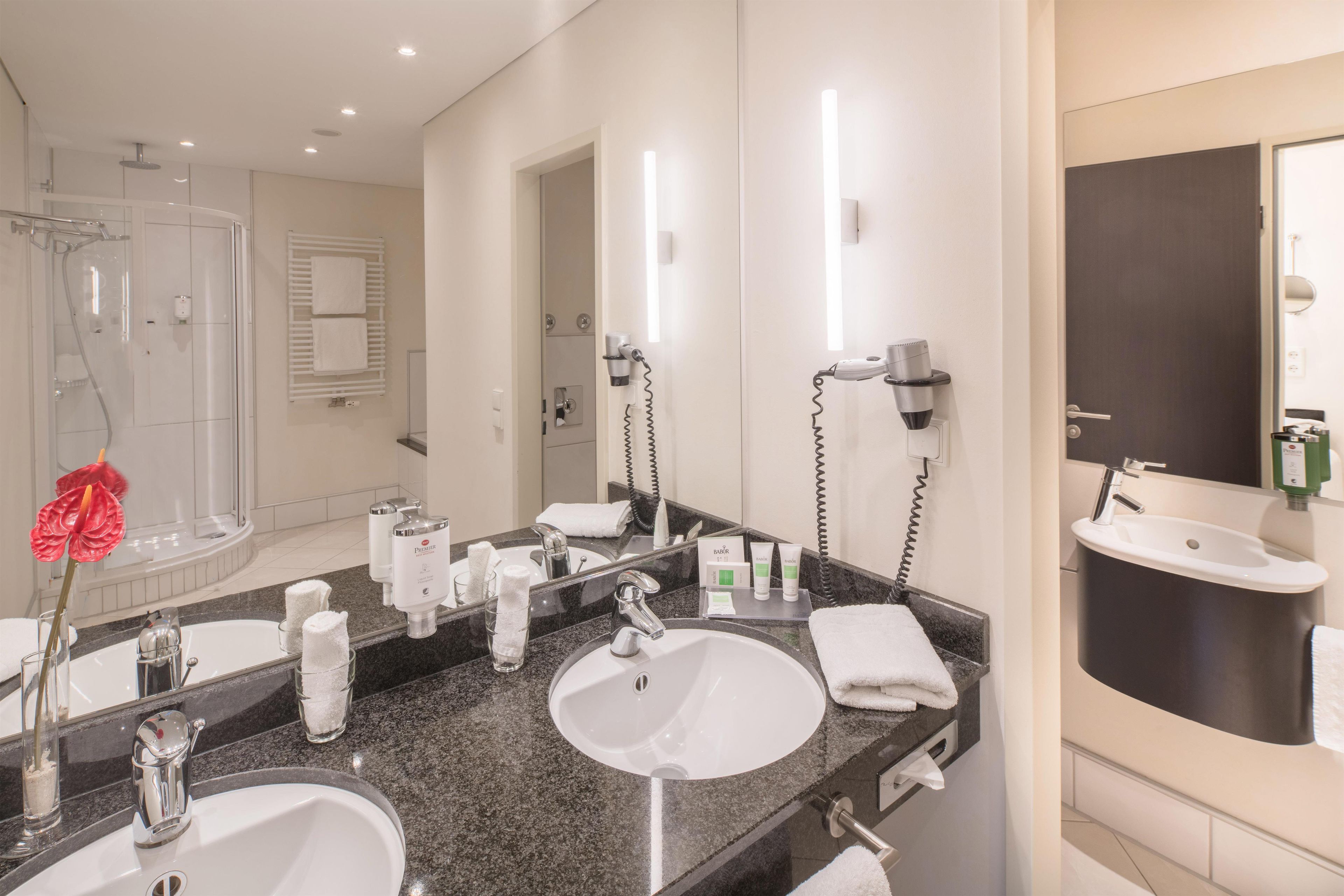 A hotel bathroom with two sinks, a shower, and a large mirror.