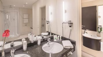 A hotel bathroom with two sinks, a shower, and a large mirror.