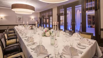 A long banquet table set for a formal event with white tablecloths, silverware, and candles.