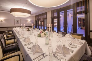 A long banquet table set for a formal event with white tablecloths, silverware, and candles.