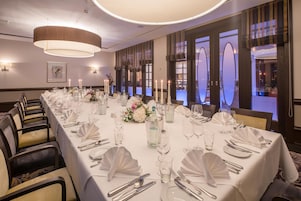 A long banquet table set for a formal event with white tablecloths, silverware, and candles.