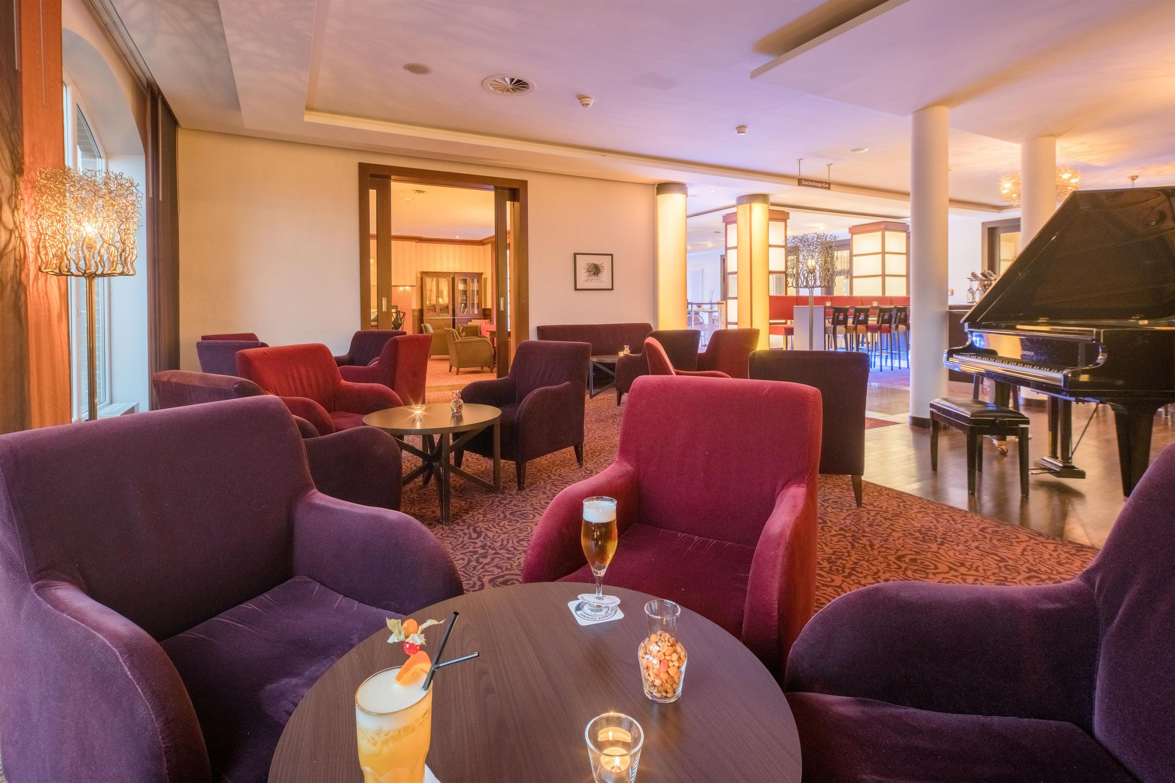 Un salón de hotel con sillones morados, un piano y una zona de bar.