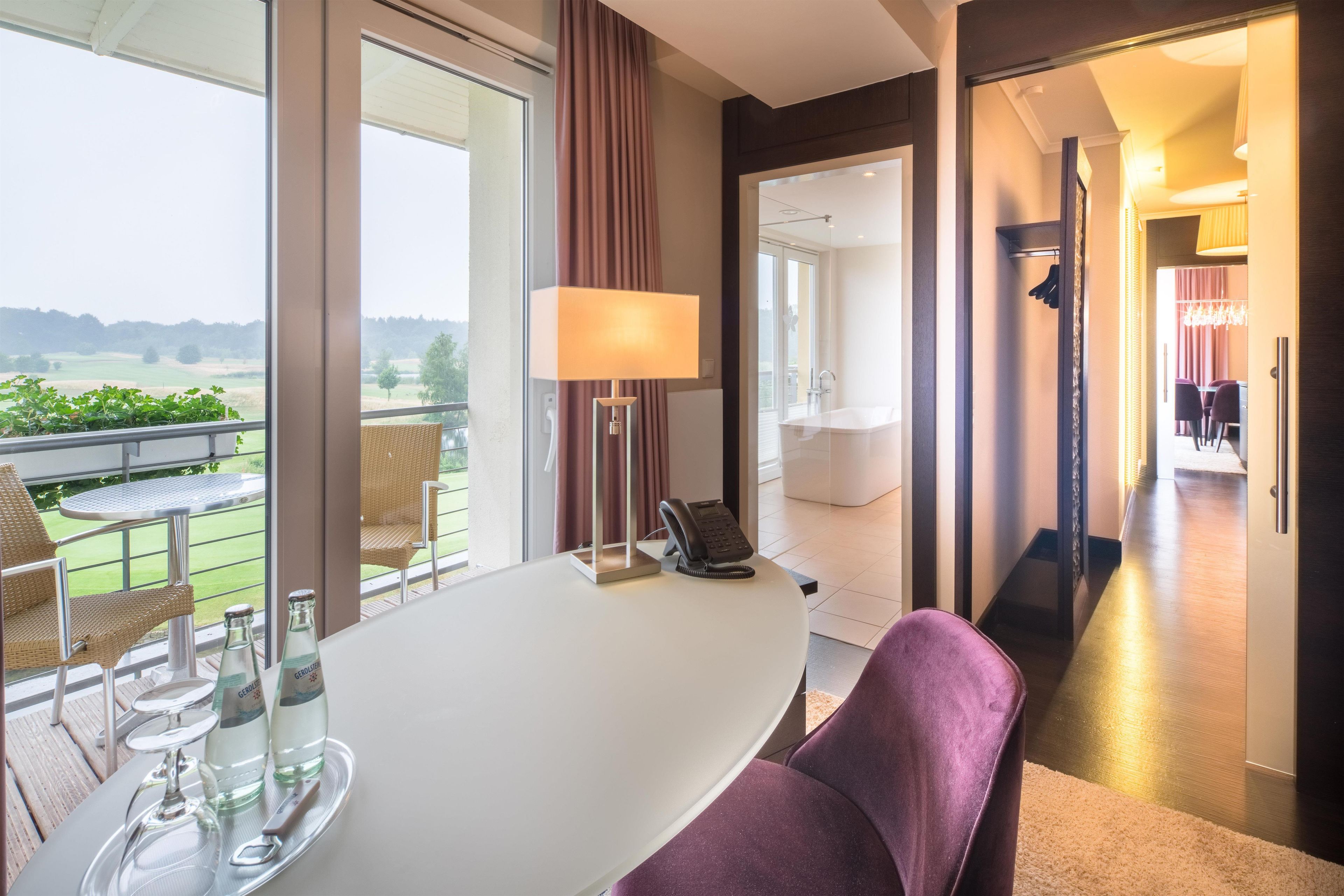 A hotel room with a balcony, a dining area, and a view of the countryside.