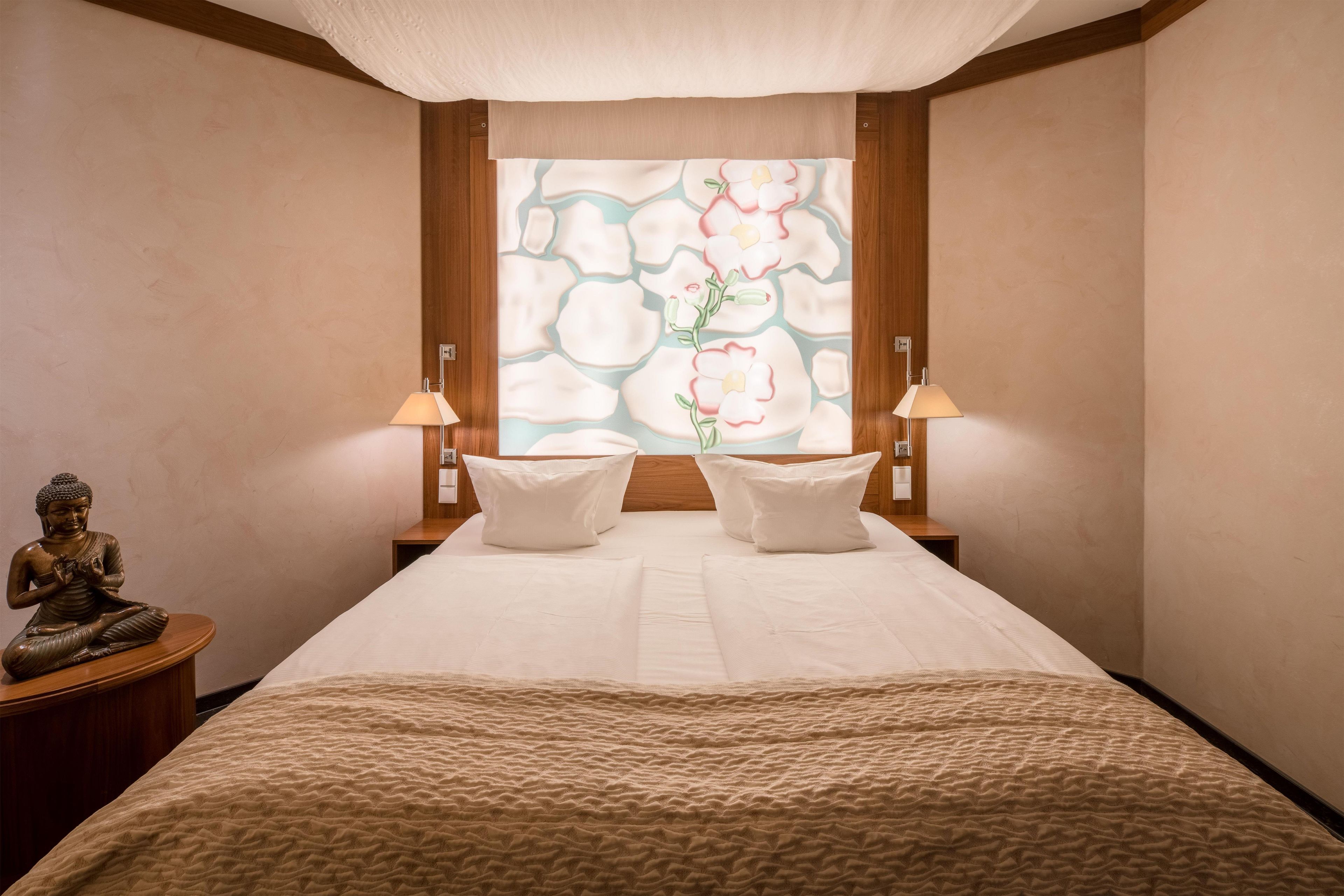 Un dormitorio con una cama, dos lámparas de noche, una estatua y una ventana con motivos florales.
