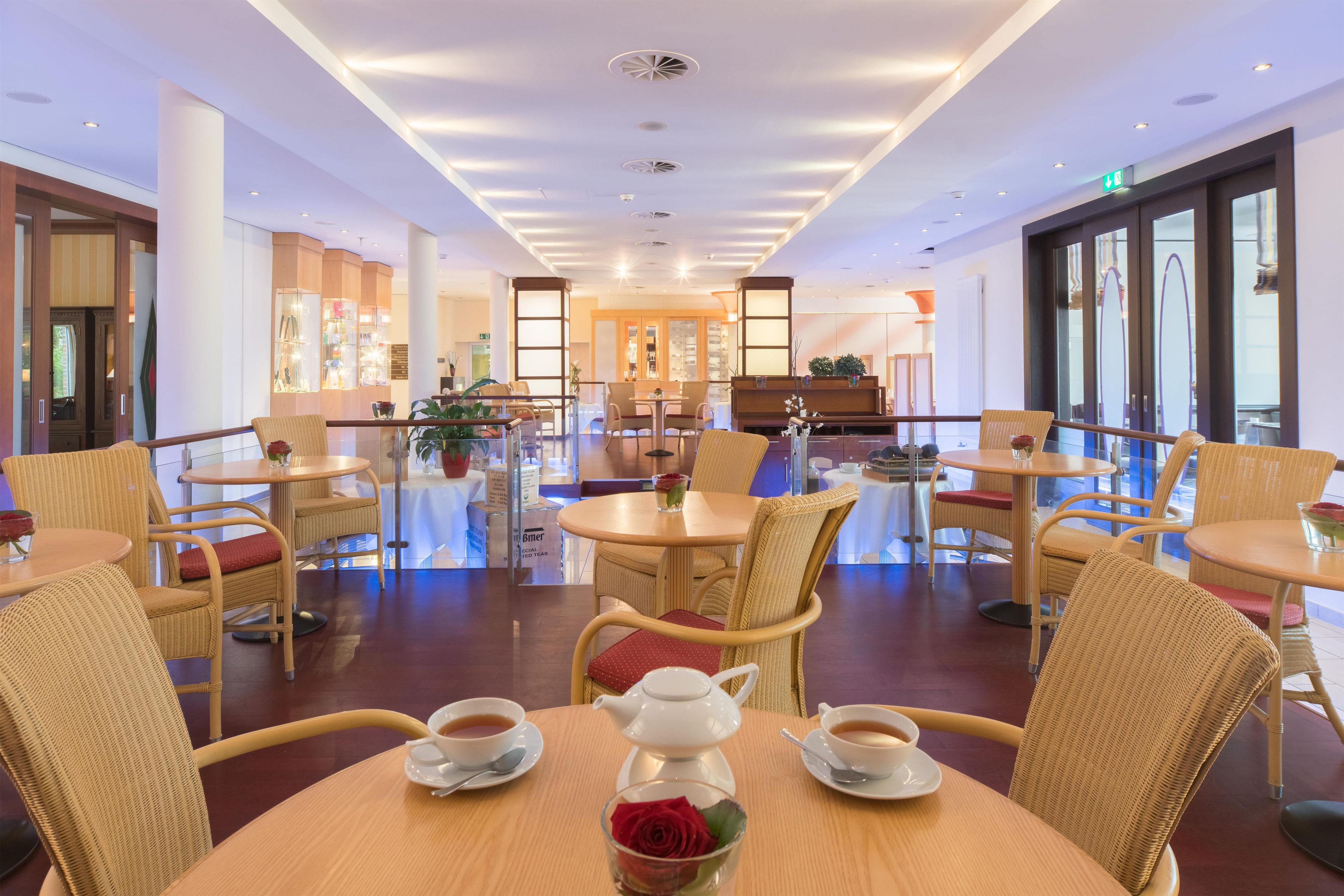 A hotel lobby with round tables, wicker chairs, and a central seating area with a tea set.