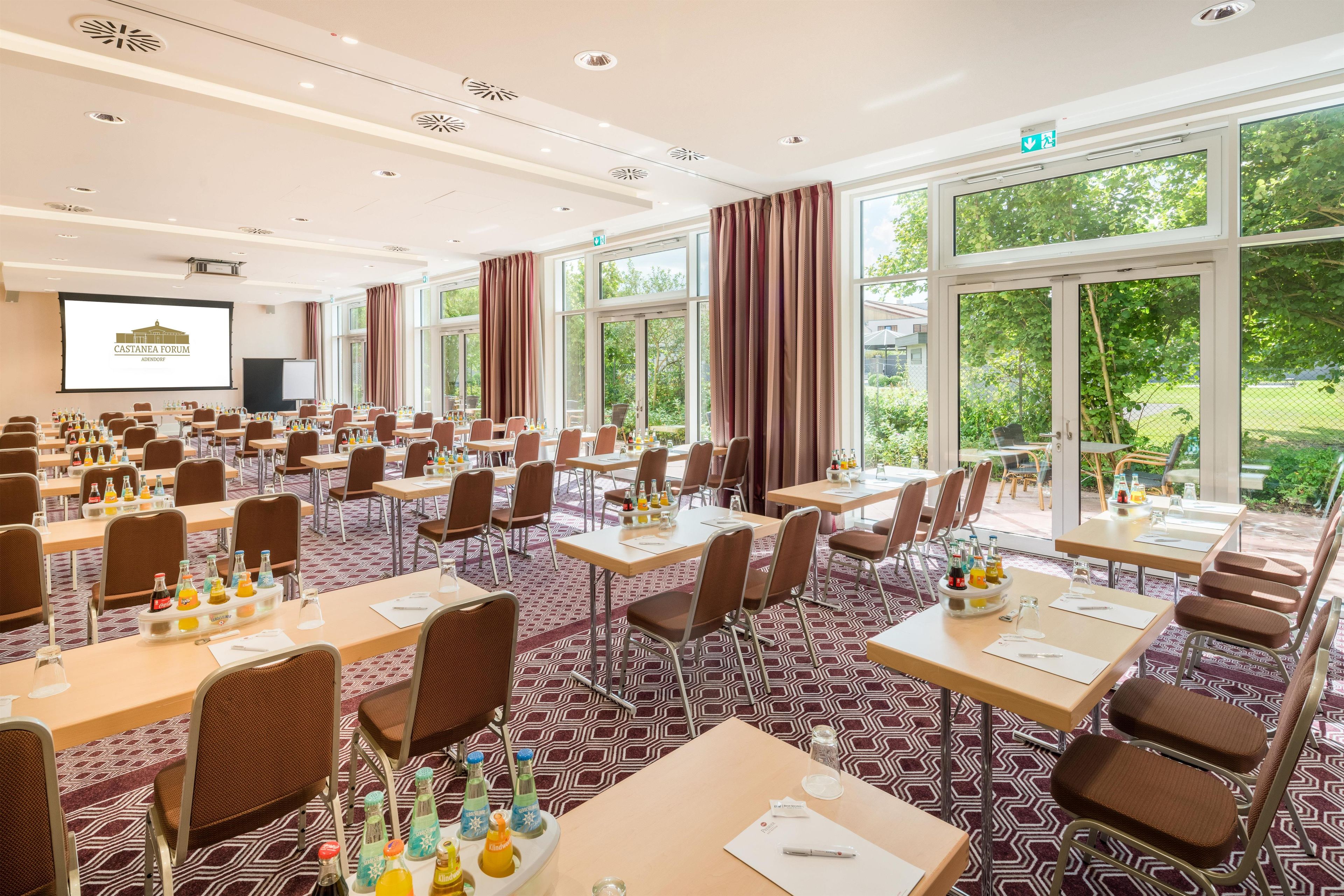 Een congreszaal met meerdere tafels, stoelen en een presentatiescherm.