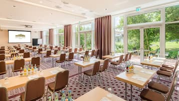 Een congreszaal met meerdere tafels, stoelen en een presentatiescherm.