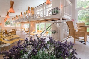 Un vestíbulo de hotel de varios niveles con una escalera, sillones y lámparas colgantes.