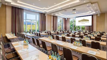 Ein Konferenzraum mit mehreren Tischen, Stühlen und einem großen Bildschirm, der 'CASTANEA FORUM ADENDORF' anzeigt.