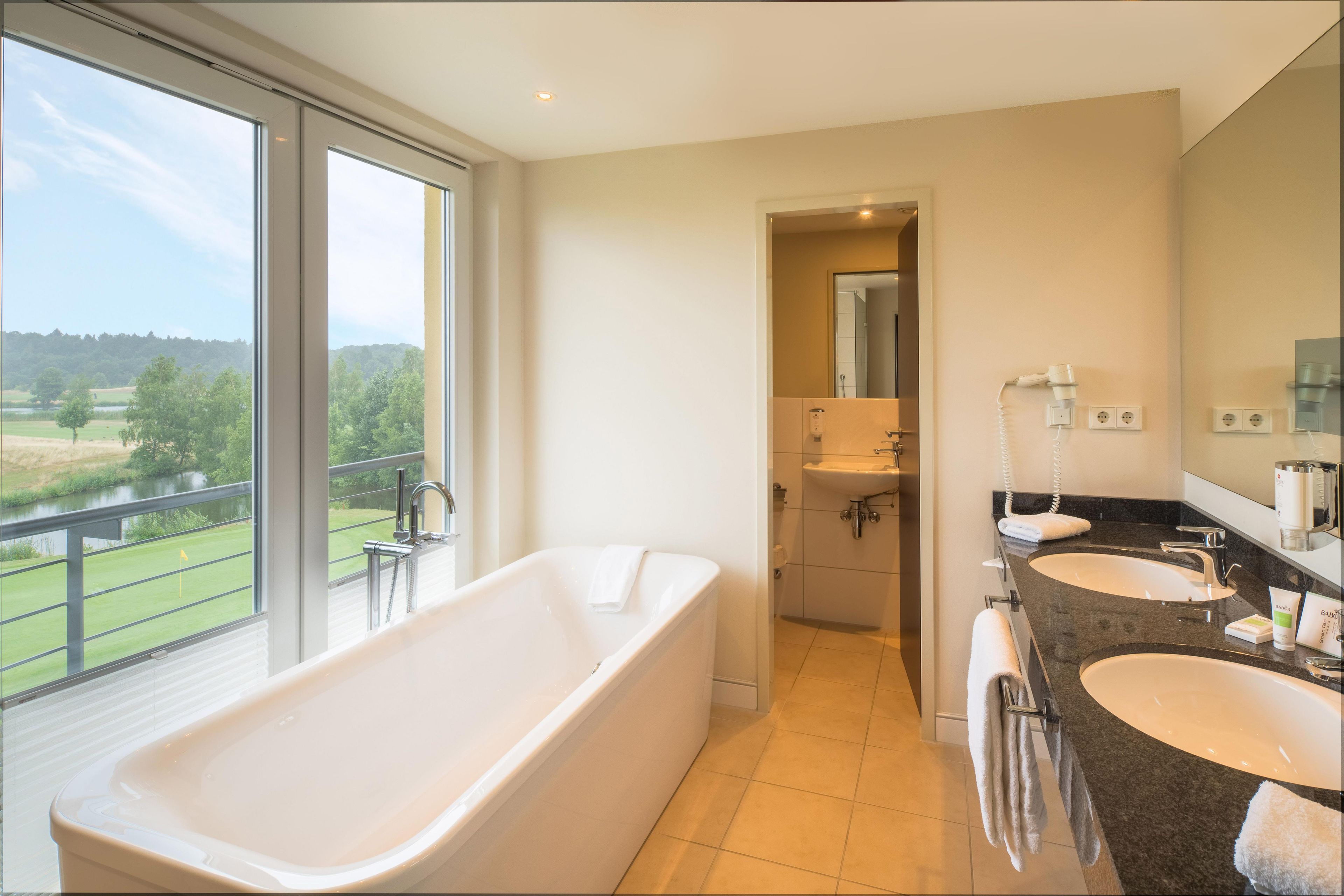 Un baño moderno con una bañera grande, dos lavamanos y vistas a un campo de golf.