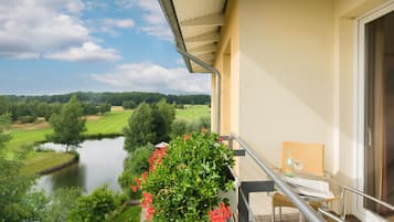 A balcony with a view of a lake and golf course, a chair, and a table with a bottle and glass.