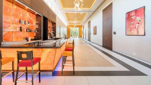 Un moderno vestíbulo de hotel con una zona de bar que presenta una barra de mármol, taburetes y una variedad de botellas y vasos.