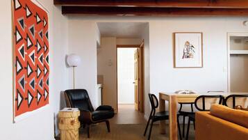 A room with a dining table, chairs, a sofa, a lamp, and a wall with a geometric pattern.