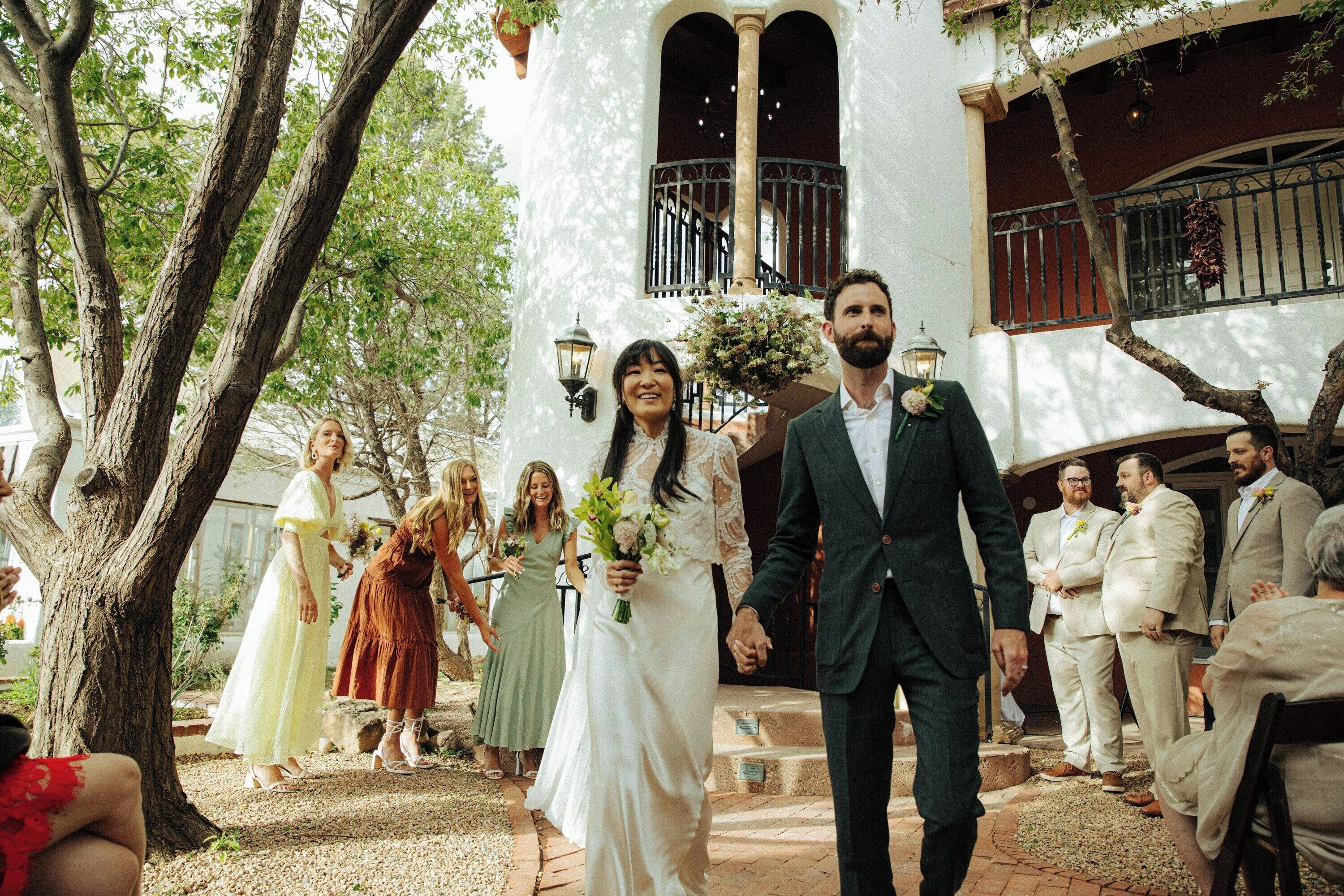 A wedding ceremony outdoors with guests and a white building in the background.