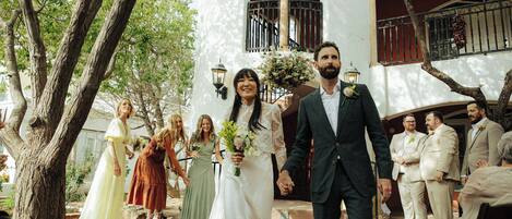 A wedding ceremony outdoors with guests and a white building in the background.