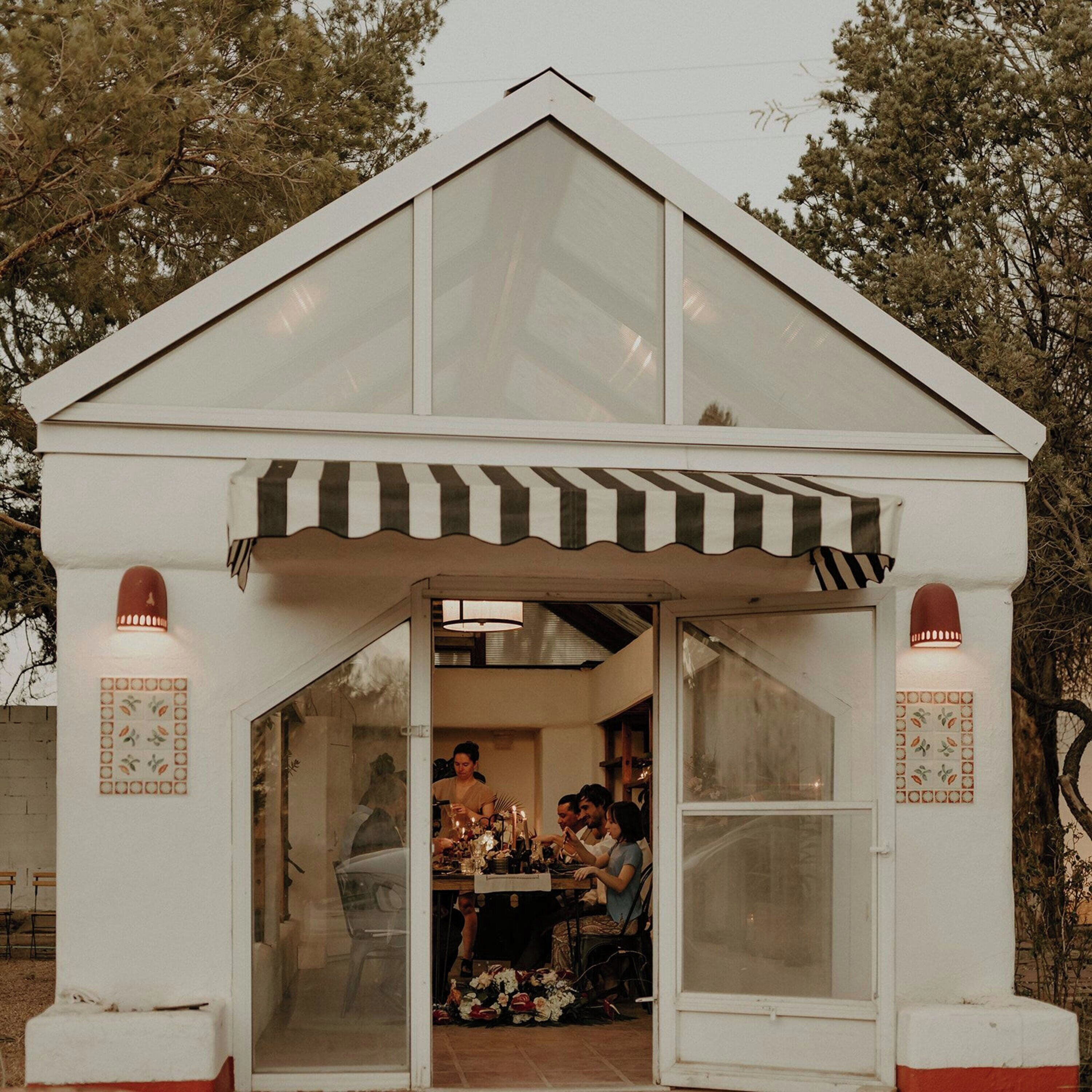 A small, white, single-story structure with a peaked roof and a striped awning.