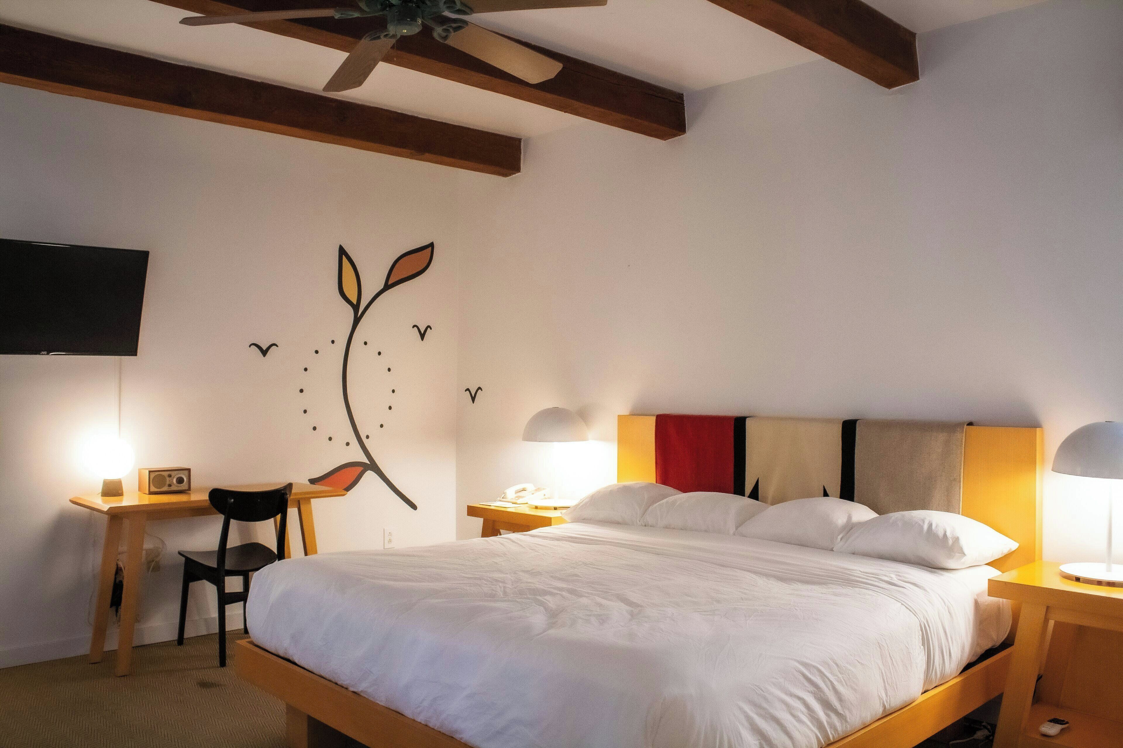 A hotel room with a bed, desk, chair, and a wall decoration.