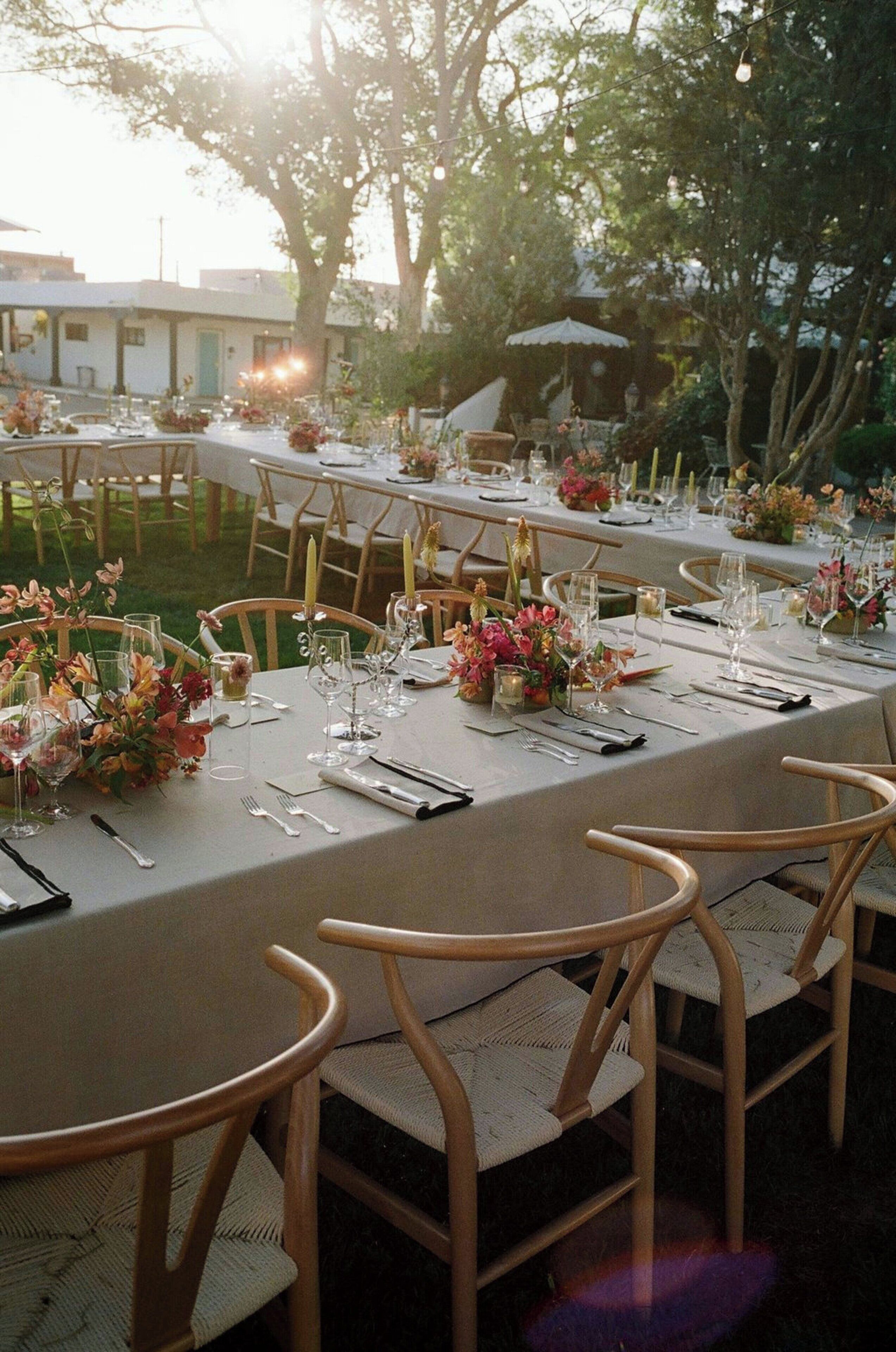 An outdoor dining area with tables set for a meal, surrounded by chairs and decorated with flowers.