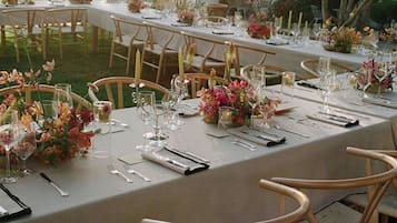 An outdoor dining area with tables set for a meal, surrounded by chairs and decorated with flowers.