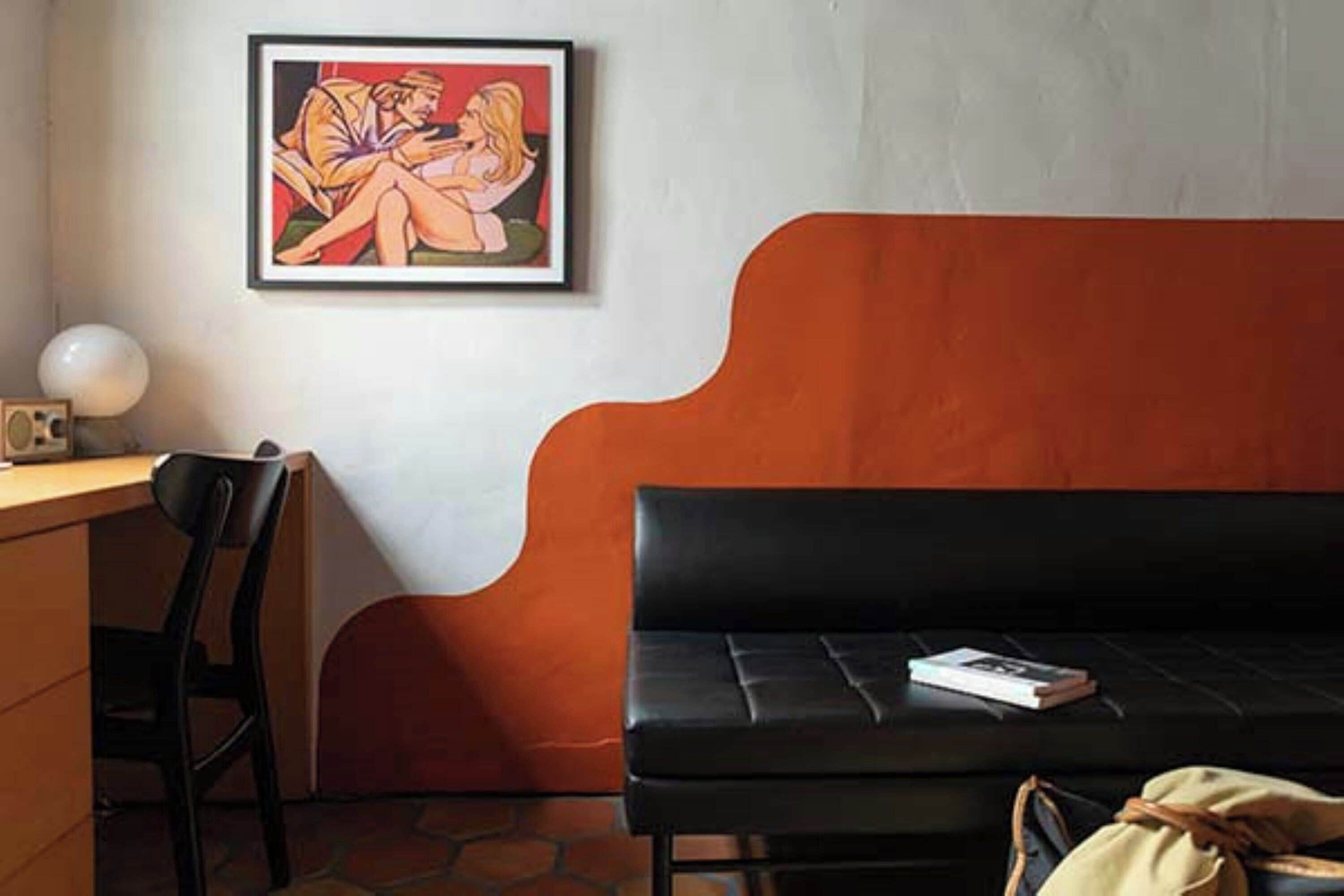 A room with a black sofa, a framed painting on the wall, a desk with a lamp, and a book on the sofa.