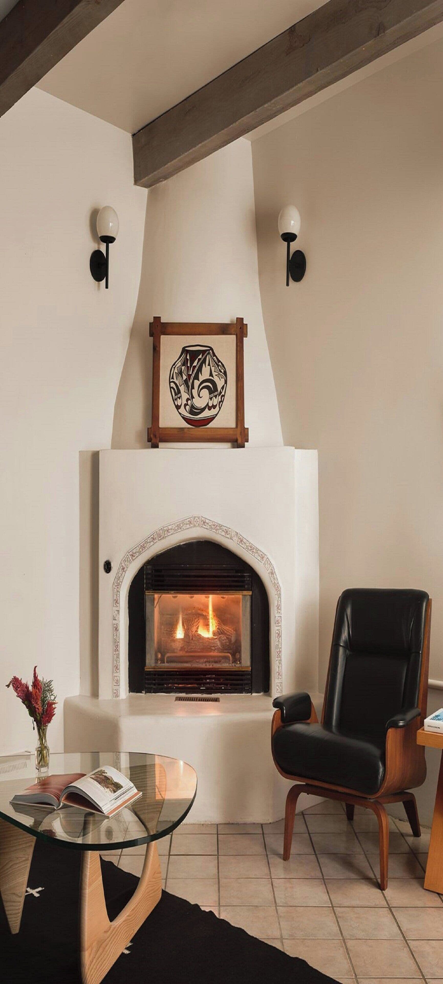 Een woonkamer met een open haard, een zwarte leren fauteuil, een glazen salontafel, en een kunstwerk in een lijst boven de open haard.