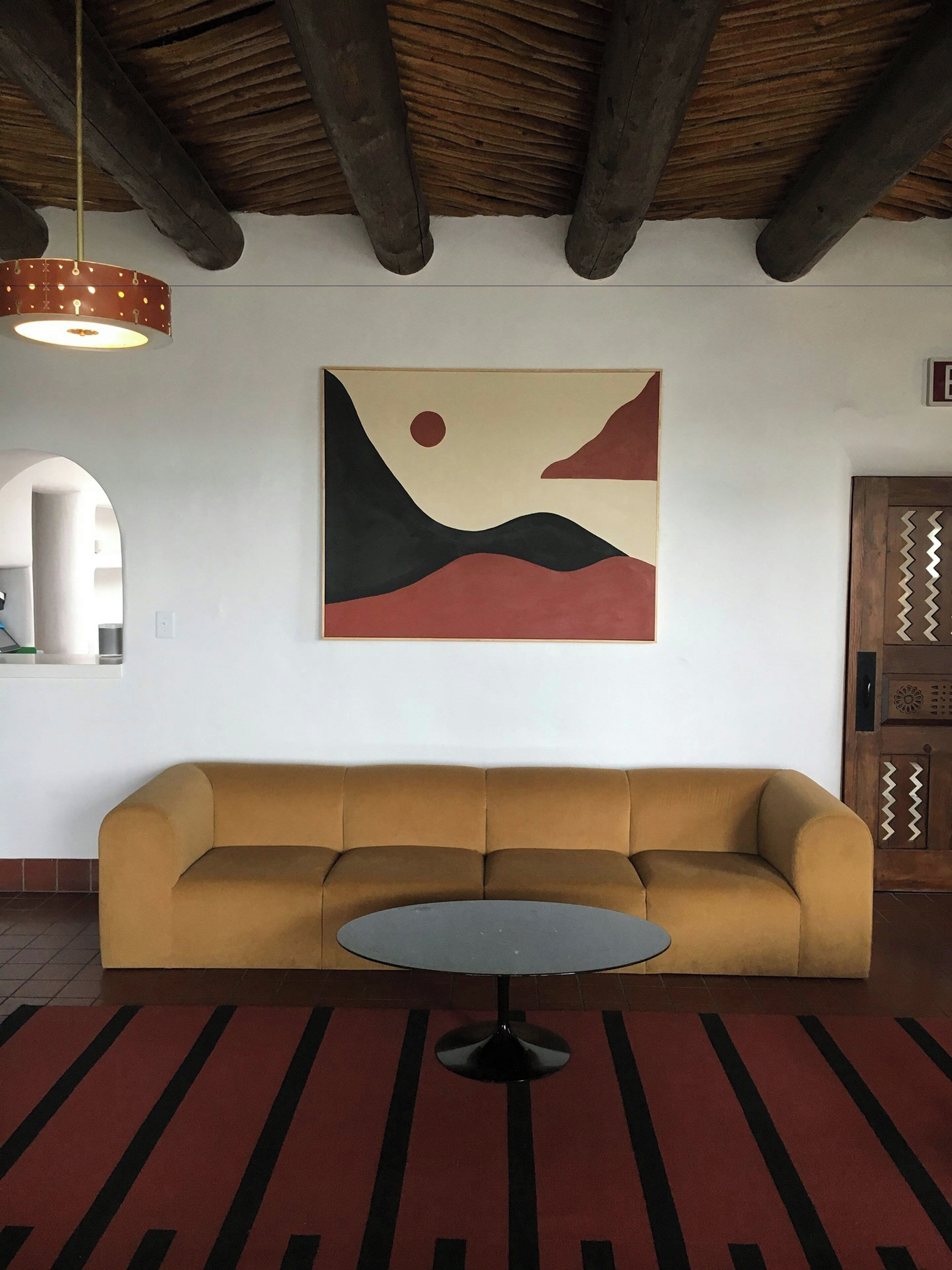 A room with a sofa, a round table, a hanging light fixture, and a wall-mounted painting.