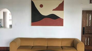 A room with a sofa, a round table, a hanging light fixture, and a wall-mounted painting.