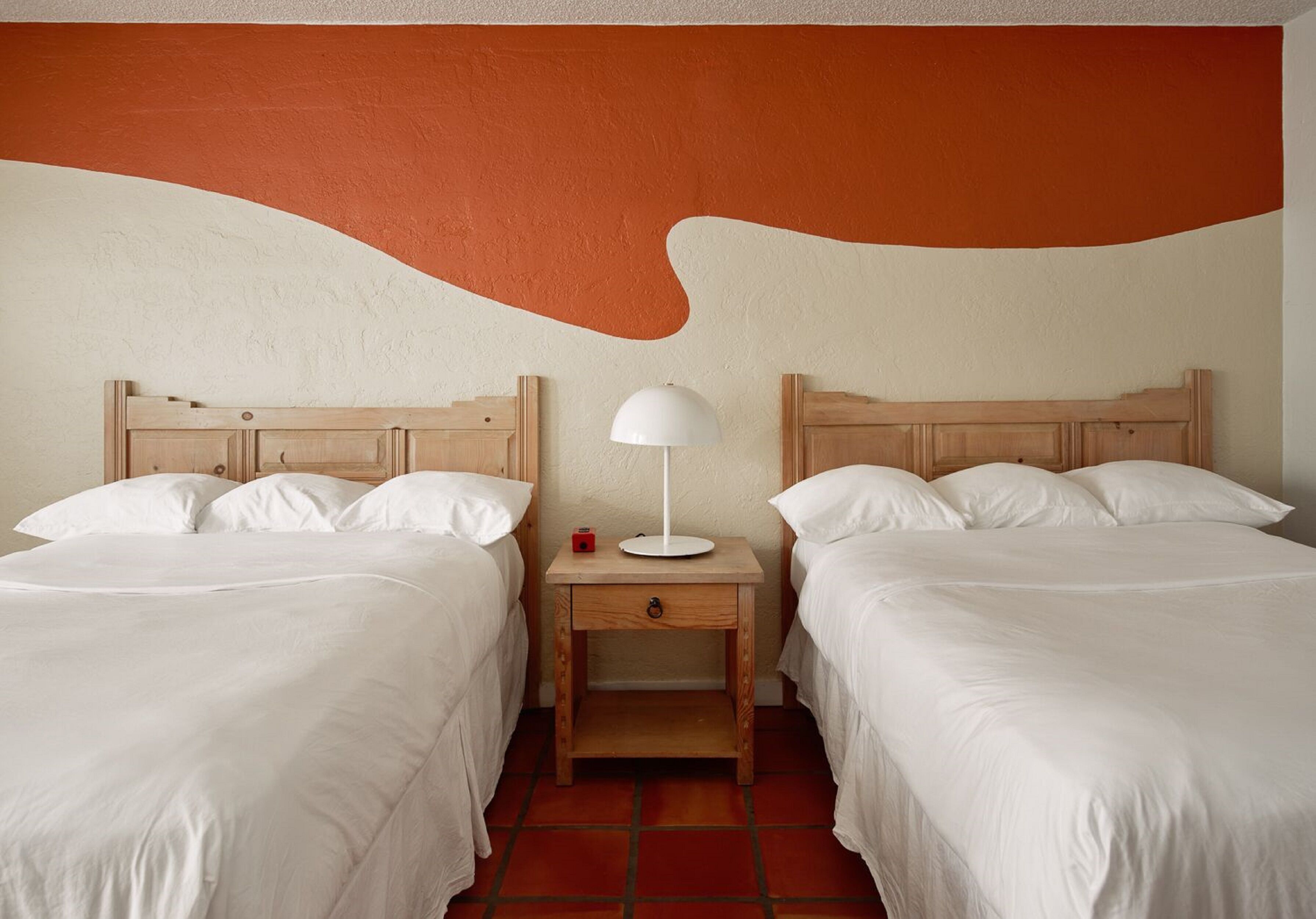 A hotel room with two beds, a nightstand with a lamp, and a wall with a large orange and white design.