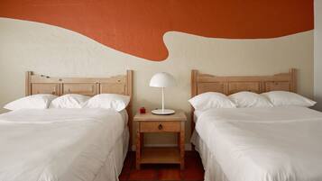 A hotel room with two beds, a nightstand with a lamp, and a wall with a large orange and white design.