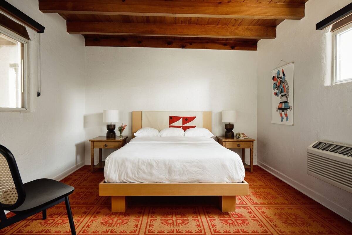 A bedroom with a wooden bed, two bedside tables, a chair, a radiator, and a window.