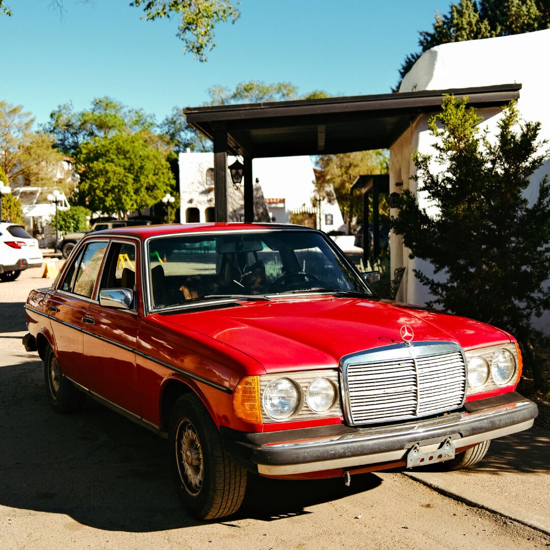 A red vintage car parked in front of a building with a covered entrance.