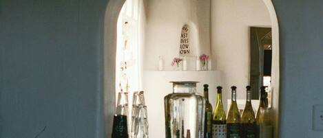 Una zona de bar con techo de madera y pared blanca. Hay botellas y vasos sobre la barra.