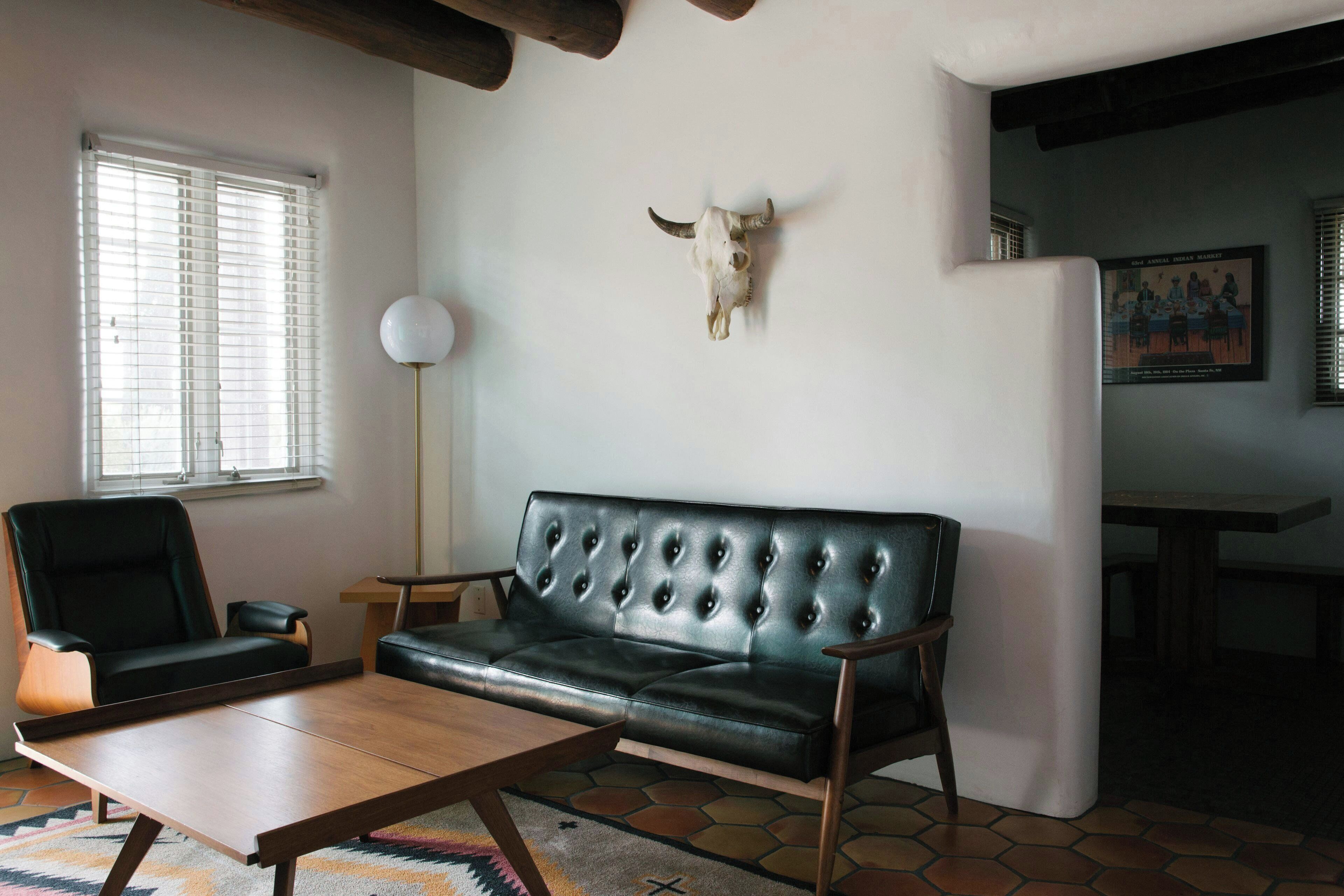 Una sala de estar con un sofá de cuero, una mesa de centro de madera, un sillón negro, una lámpara de pie y una decoración con cráneo de toro.