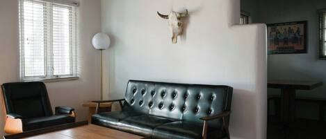 Una sala de estar con un sofá de cuero, una mesa de centro de madera, un sillón negro, una lámpara de pie y una decoración con cráneo de toro.