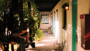 A corridor with a bench, a potted plant, and a door with a light fixture. - El Rey Court (Santa Fe)