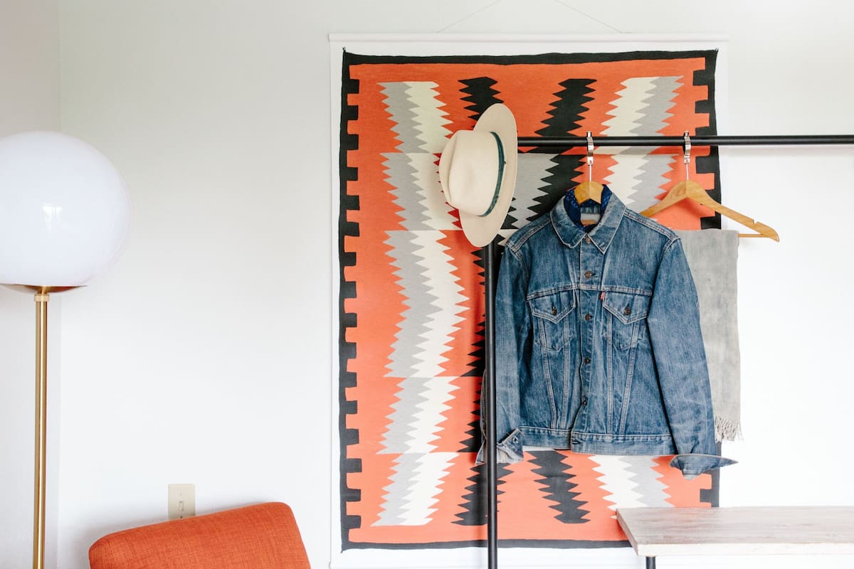 A room with a patterned rug, a hat, and a denim jacket hanging on a rod.