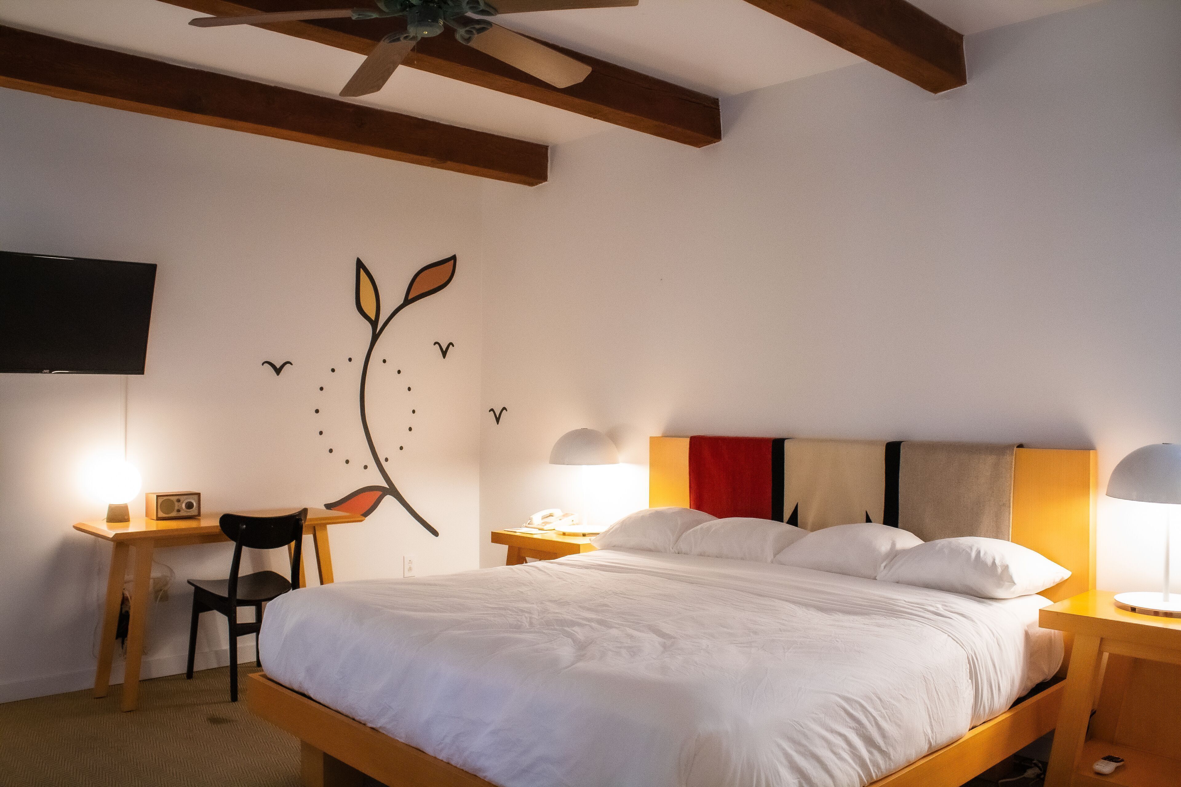 A bedroom with a bed, desk, chair, and bedside lamps.