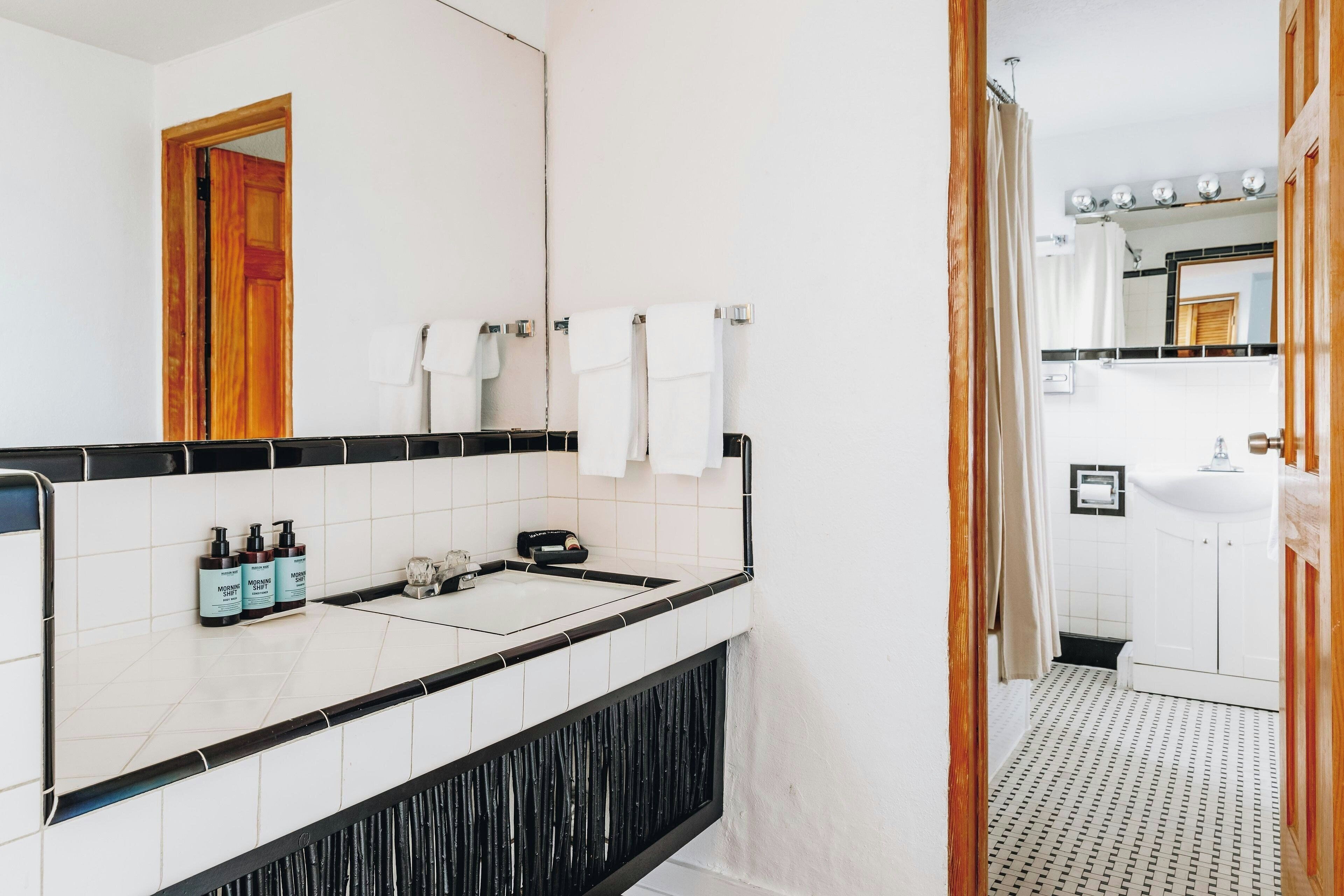 A modern bathroom with a black and white tiled vanity, a mirror, and a shower area.