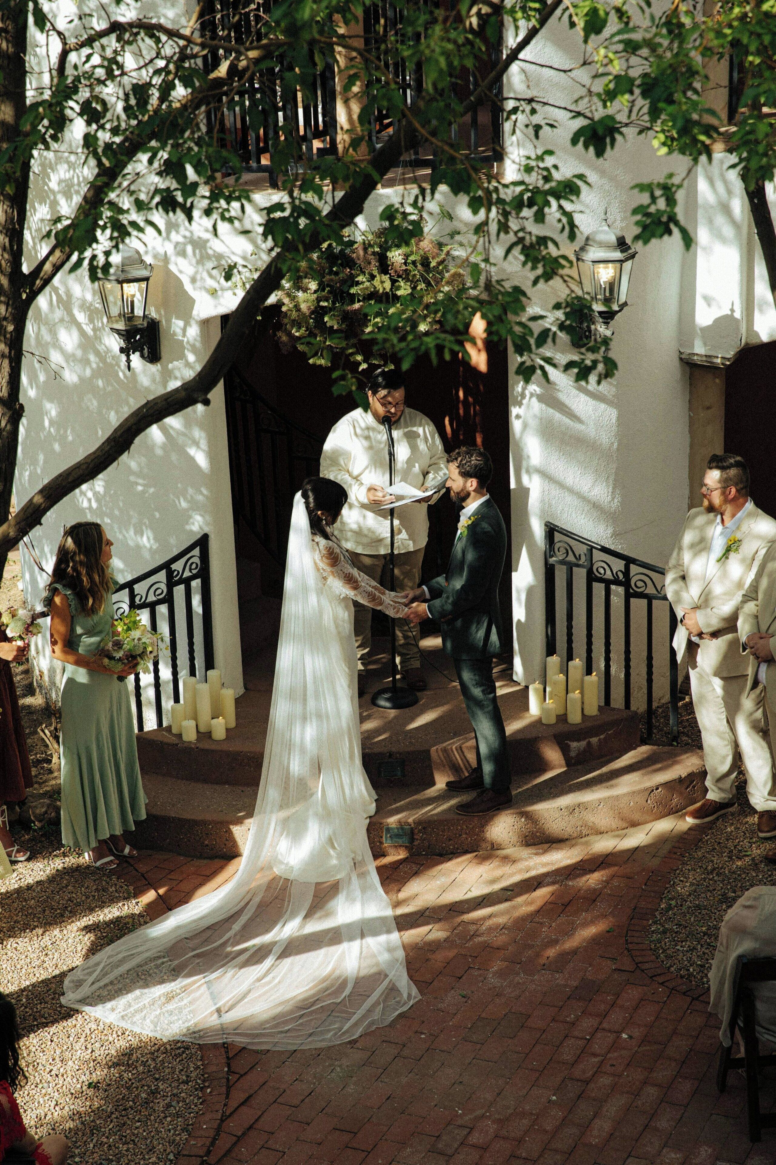 A wedding ceremony outdoors with a bride in a white dress and groom in a dark suit.