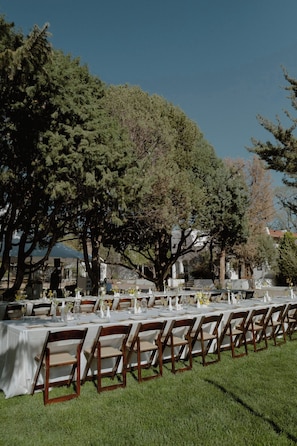 Un área de comedor al aire libre con mesas dispuestas para los huéspedes, rodeada de árboles y un cielo despejado.