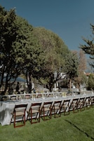 Un área de comedor al aire libre con mesas dispuestas para los huéspedes, rodeada de árboles y un cielo despejado.