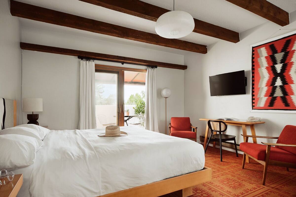 A hotel room with a bed, a desk, two chairs, a TV, and a large window.